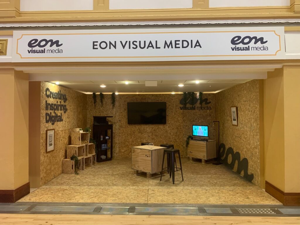 Eon Visual Media's stand at The Business Day. Showing a blank set up of plain wood with the eon logo and slogan spray painted across the walls. 